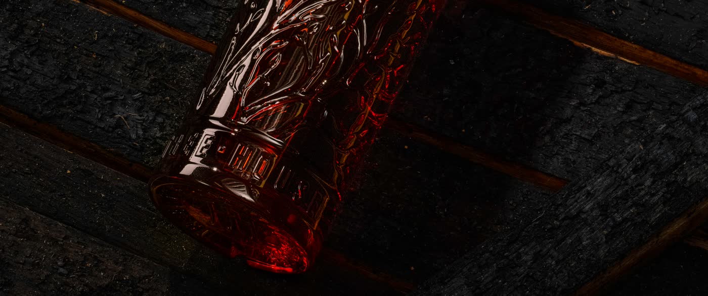 A KOLA bottle resting on charred barrel staves